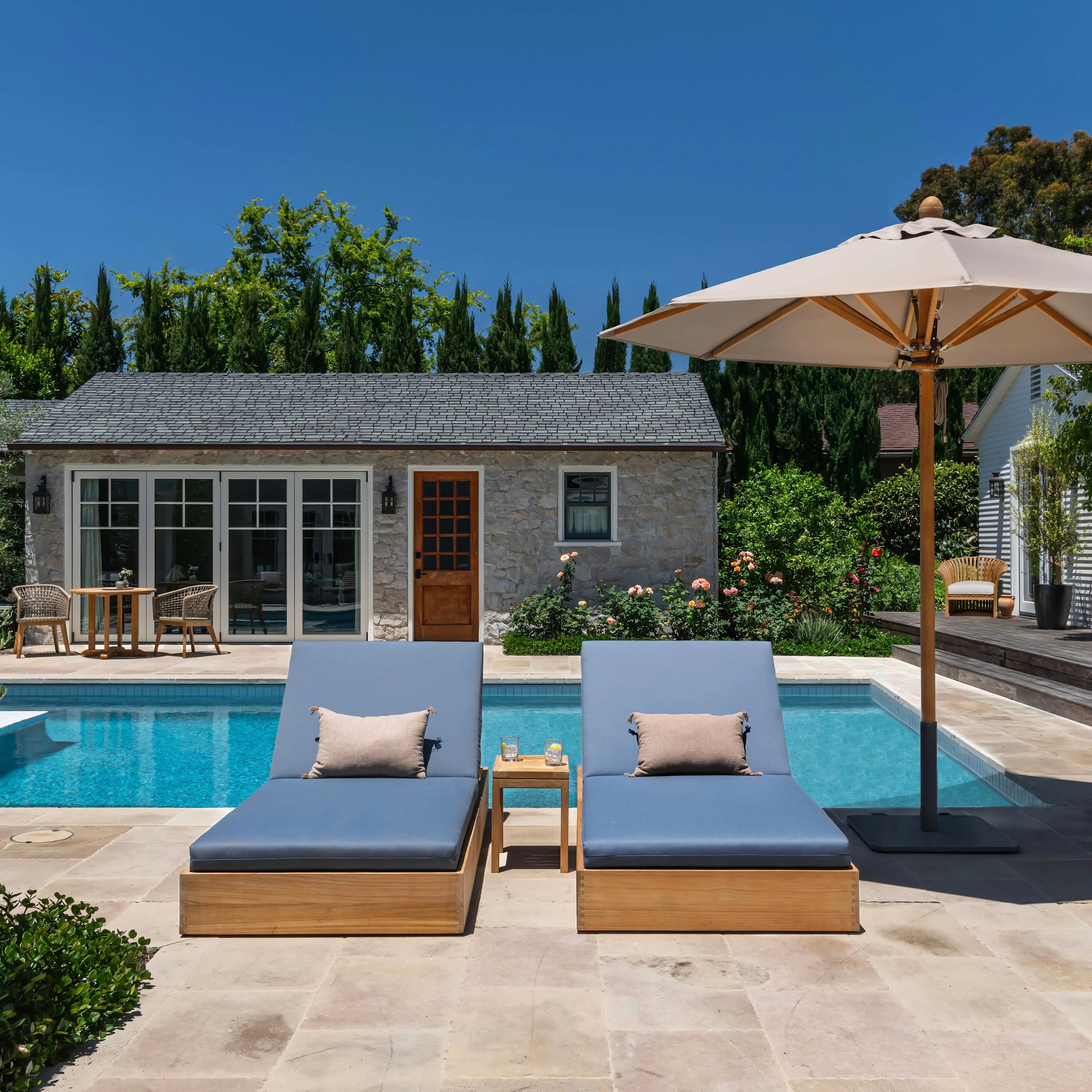 Outdoor poolside chaise lounges with pillows and umbrella