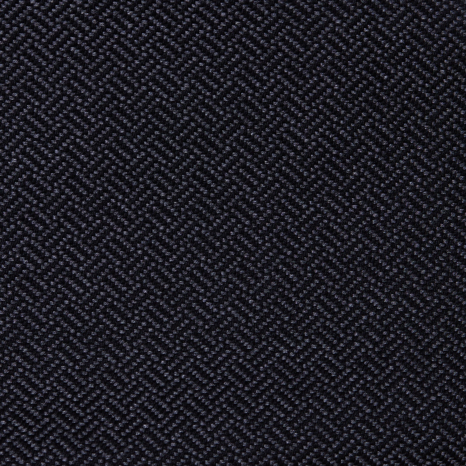 Dark fabric displaying a textured, small herringbone pattern, creating a repeating zigzag effect. The tightly woven threads form a tactile surface, suggesting a sturdy material in close-up. No text visible.