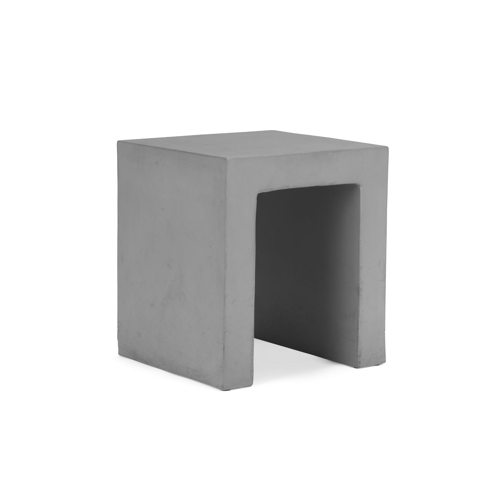 A gray, cuboid concrete stool rests on a white surface, featuring an open bottom and a smooth, minimalist design in a plain, well-lit setting.