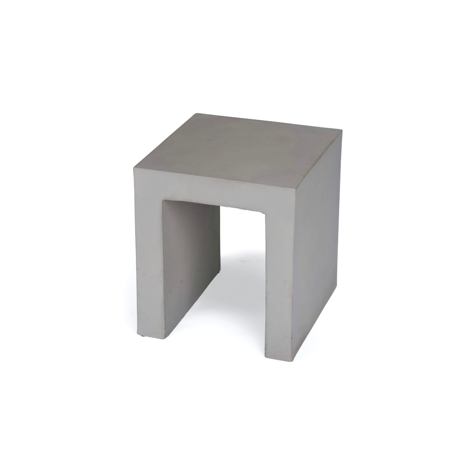 A minimalist, square-shaped concrete stool stands upright, featuring a hollow base. It's set against a plain white background, emphasizing its clean lines and geometric design.