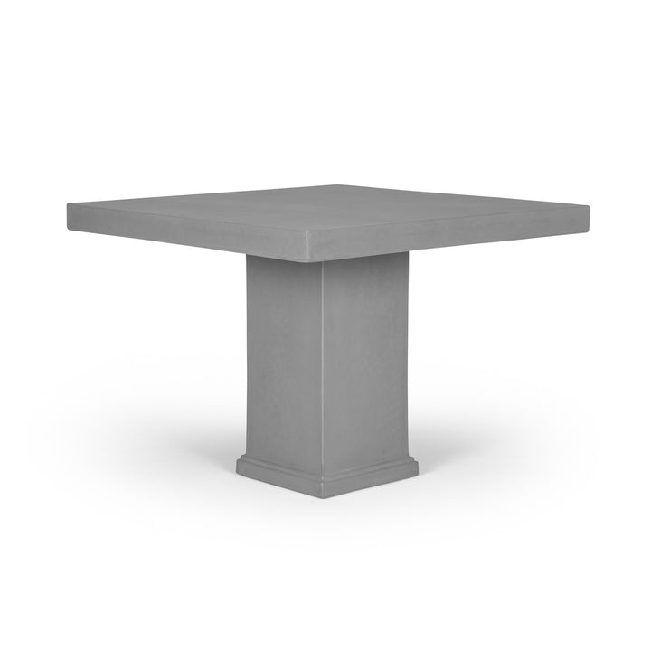 A square, grey table with a thick, central pedestal base is positioned against a plain white background, emphasizing its modern, minimalist design.