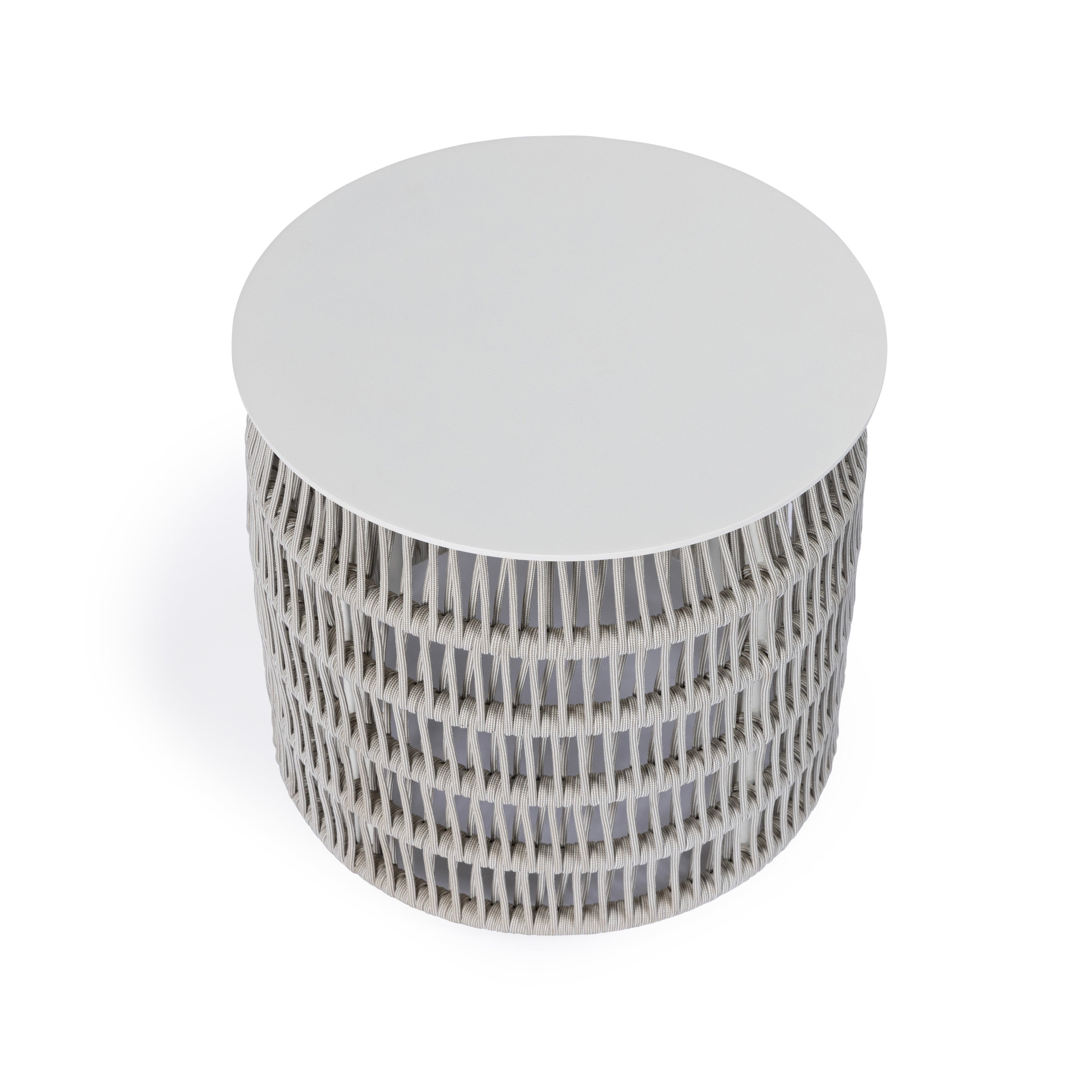 A round, white table with a woven textured cylindrical base stands on a plain white background. The base features a crisscross pattern, creating a modern, minimalist appearance.