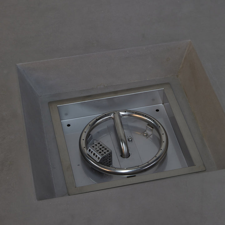 A chrome circle with a central handle rests within a square, recessed metal frame embedded in a concrete surface, surrounded by empty, gray space.