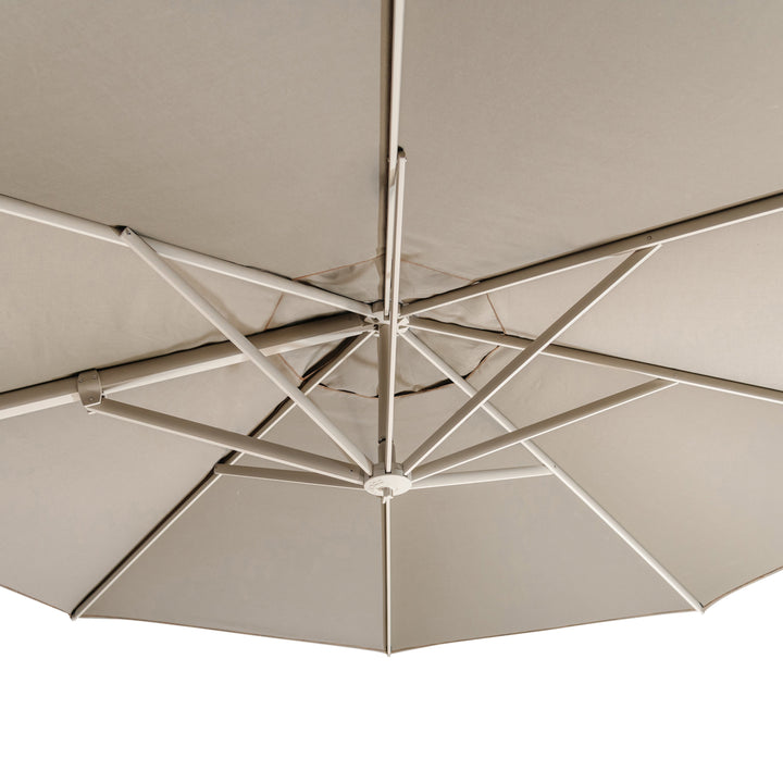 A large outdoor umbrella with a beige canopy is displayed from underneath, showing its metal rib structure and supporting beam, set against a neutral background.