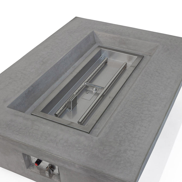 Rectangular concrete fire pit table with a stainless steel inset and control knobs, situated in a minimalist indoor setting.