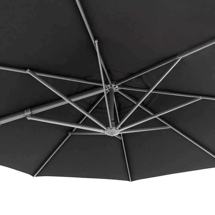 A large, dark-colored umbrella viewed from below, showing multiple metal spokes extending from the center, forming a geometric pattern against a plain backdrop.