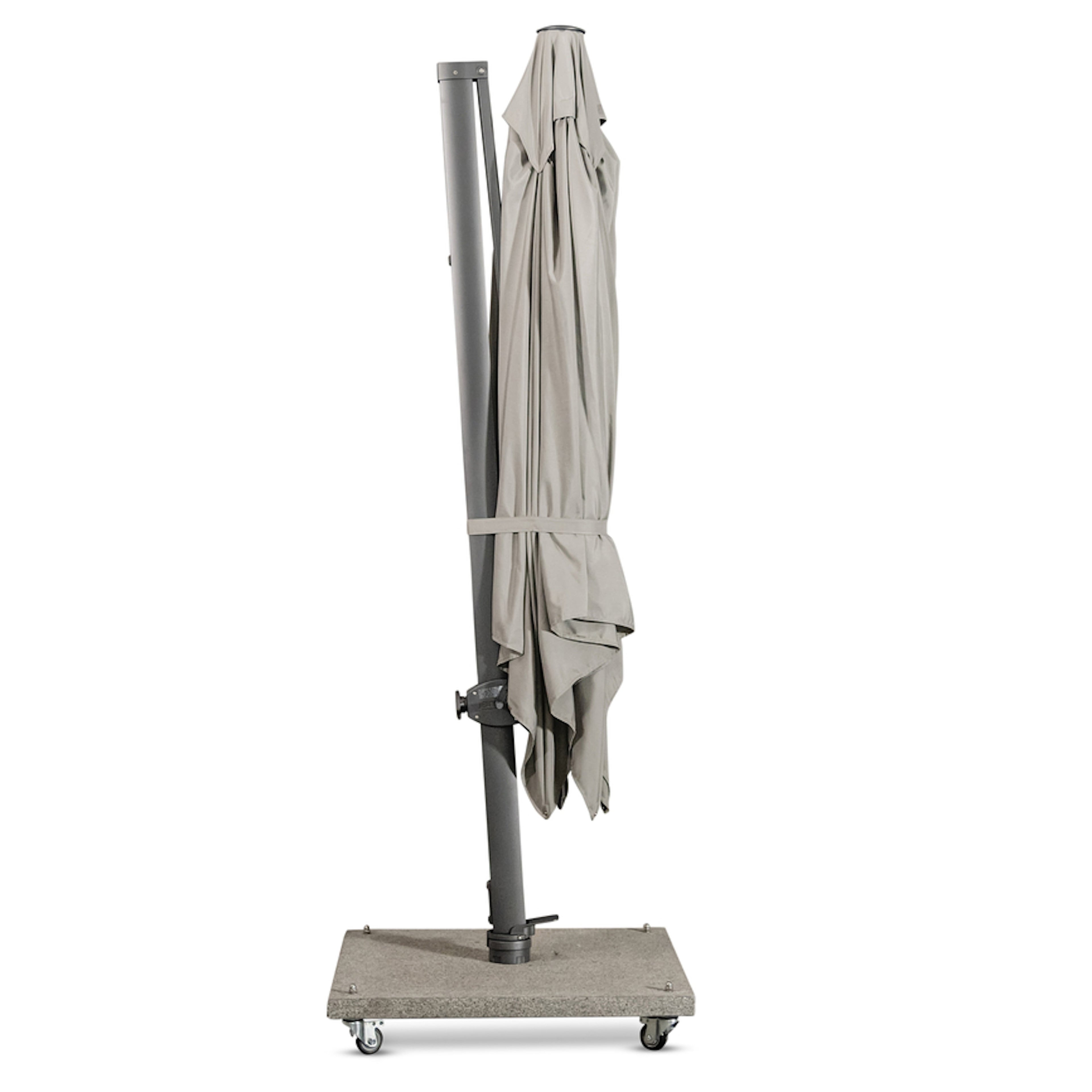 A closed, gray patio umbrella stands upright on a wheeled rectangular stone base in a gray, sparse indoor setting.