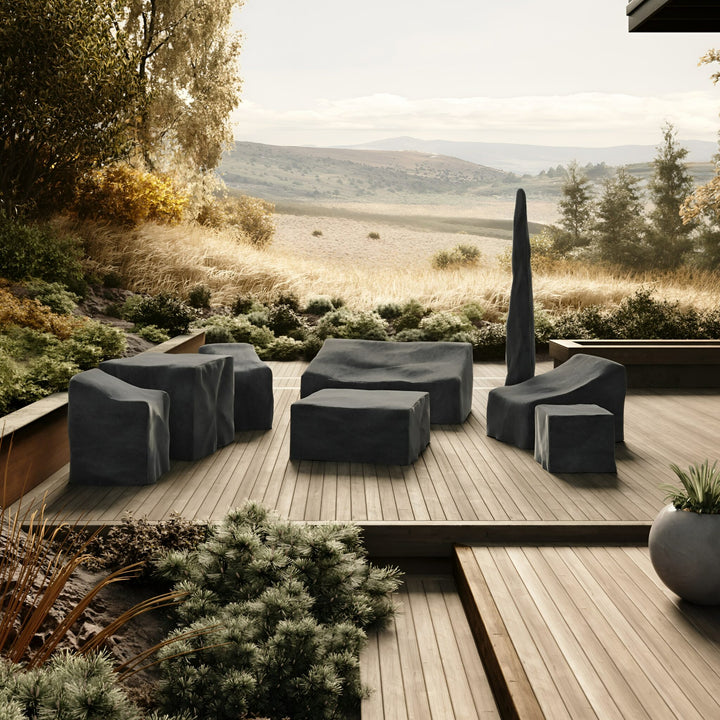 Outdoor furniture sits on a wooden deck, covered with protective covers, and surrounded by lush greenery. In the background, rolling hills and a serene landscape stretch to the horizon.