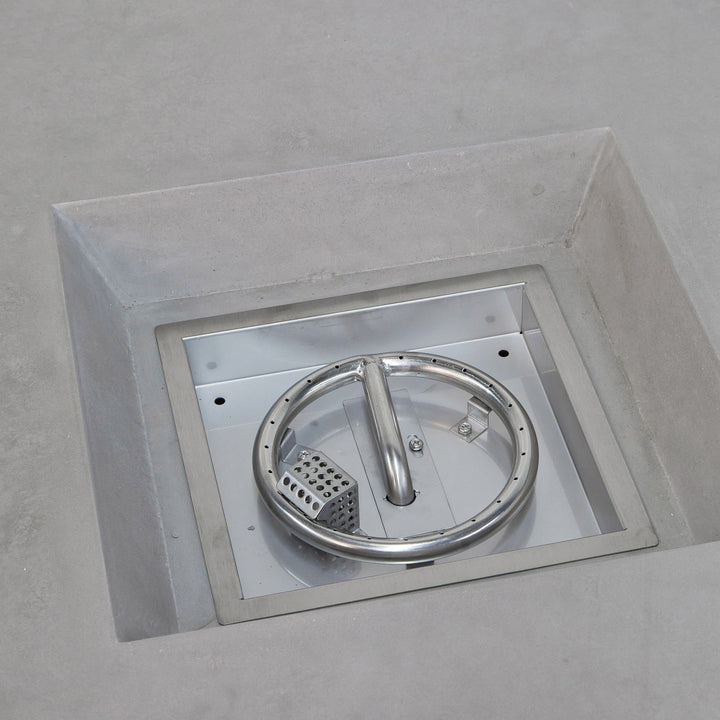 Circular metallic handle within a stainless steel square cover, recessed into a concrete surface, featuring a perforated drain and securing screws.