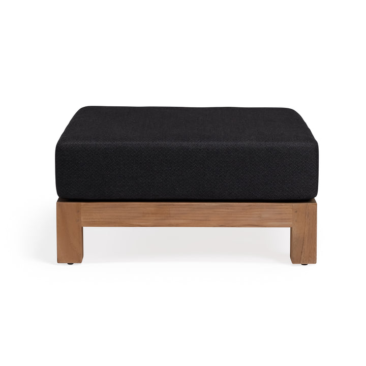 A rectangular ottoman with a black cushion rests on a wooden base, placed against a plain white background.