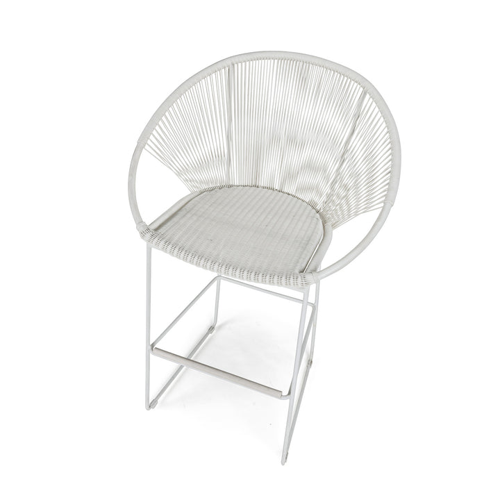 A white woven chair with a circular backrest sits on a minimal metal frame, positioned in a bright, plain setting.