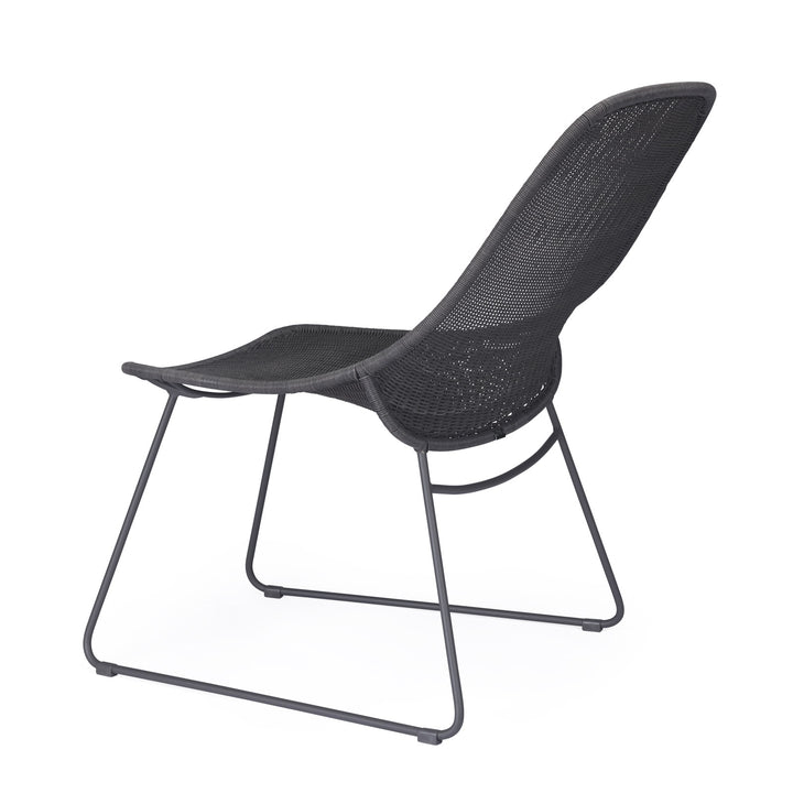 A modern, black mesh chair is positioned to the right, featuring a curved, open back and sleek metal frame, set against a plain, white background.