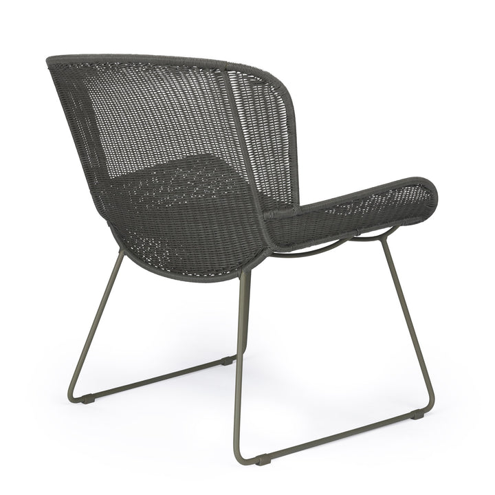 A dark, wicker chair with a metal frame stands stationary in a studio setting, highlighting its woven texture and minimalist design.