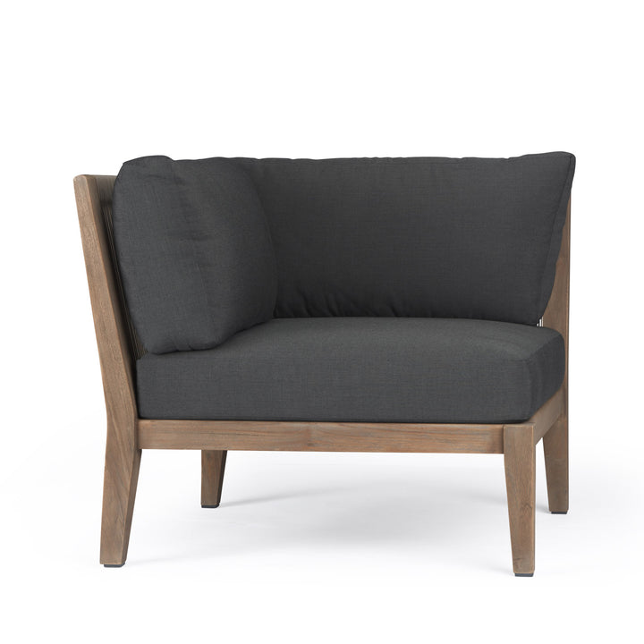 A corner sofa chair with dark gray cushions rests on a wooden frame. It is situated against a plain white background.