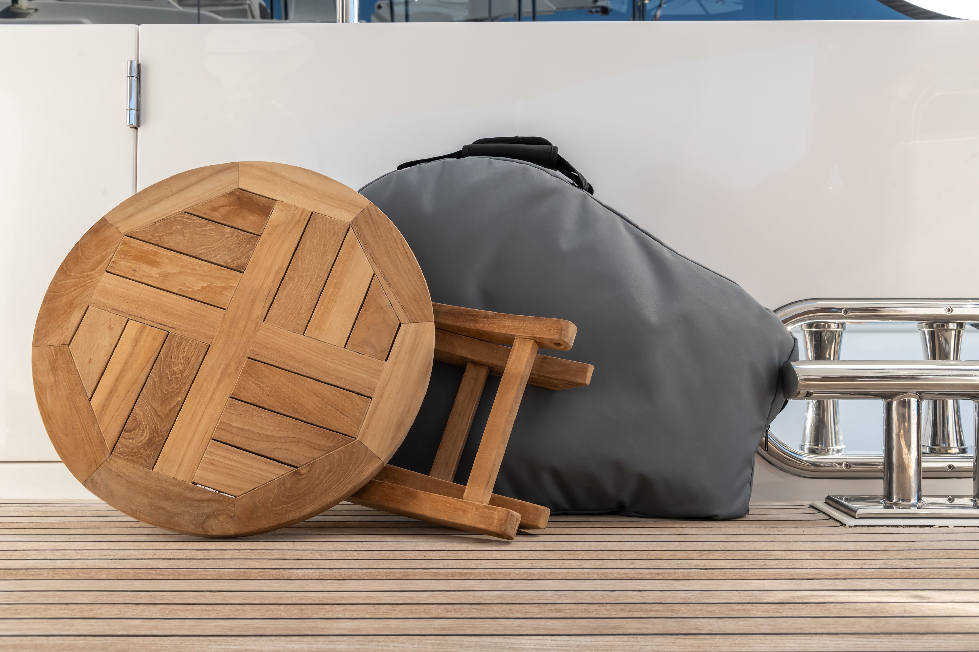 A wooden round table lies on its side against a gray padded cover, surrounded by metal railing on a wooden deck.