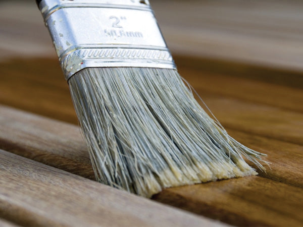 A paintbrush applies stain on wooden planks. The brush, labeled "2" 51.2mm" on its metal handle, spreads the finish, enhancing the wood's natural texture and color.