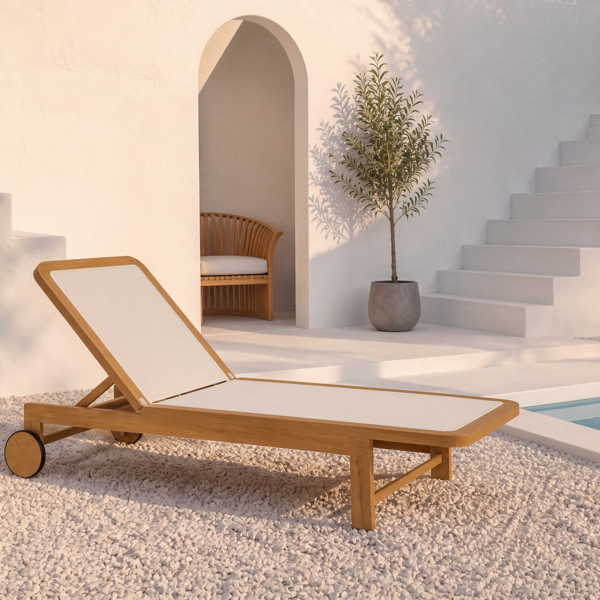 A wooden outdoor chaise lounge with white cushion fabric and small caster wheels, placed on a light stone surface beside a pool in a bright, modern patio setting with stairs, an archway, and a potted tree.