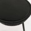 A round black stool with a smooth top and woven edge is centered above slender legs on a plain light background creating a minimalist and modern aesthetic.