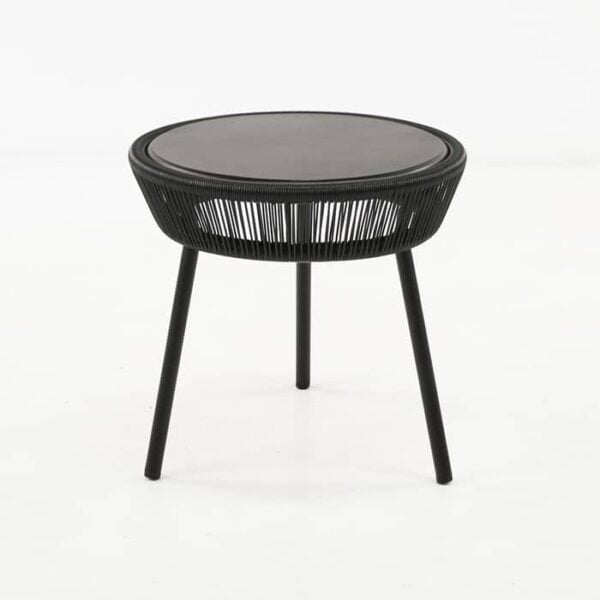 A round black table with a smooth top and a woven design on the sides stands on three slender legs in a minimalistic white space.